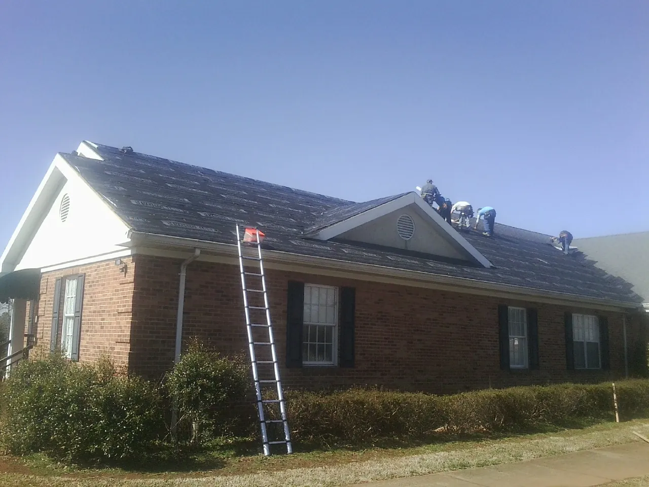Crew tearing shingles off a brick ranch roof with a ladder set — Emergency Roof Repair work by our crew in Abington