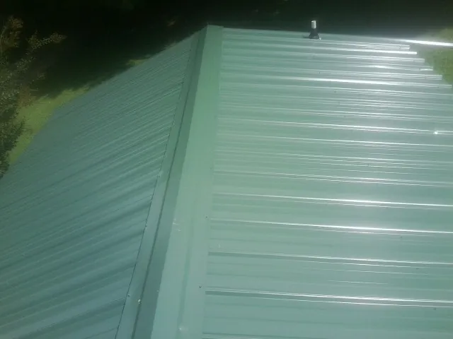 New green metal panels meeting at the ridge of a roof — Flat Roof Repair work by our crew in Abington