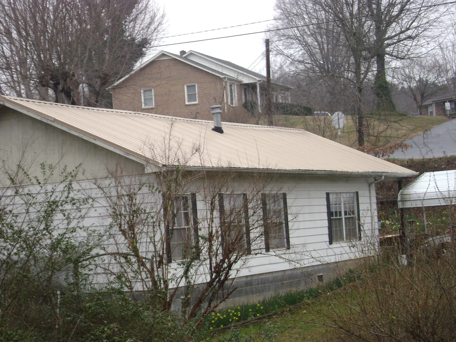 Tan metal roof on a white sided house set into a hillside — Commercial Roofing by Roofing Brothers in Abington
